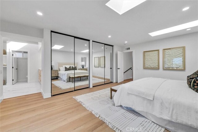 bedroom with recessed lighting, visible vents, light wood-type flooring, a skylight, and two closets