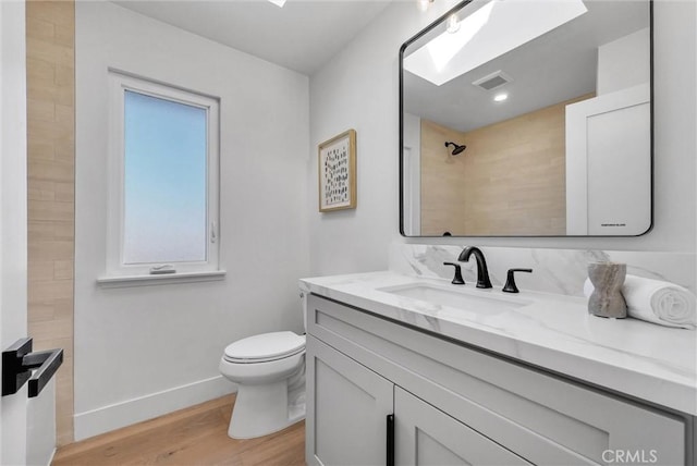 bathroom with vanity, wood finished floors, visible vents, tiled shower, and toilet