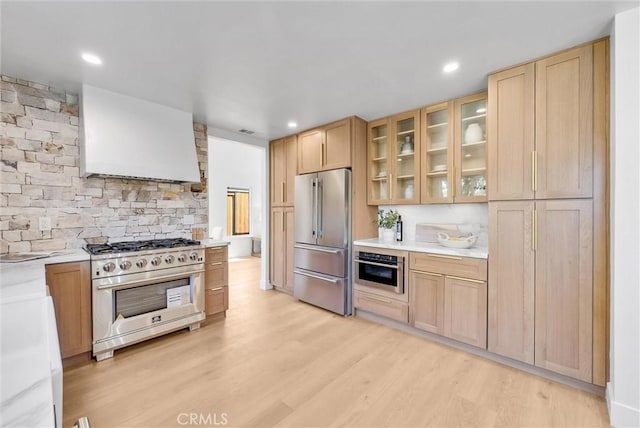 kitchen featuring exhaust hood, premium appliances, light countertops, light brown cabinets, and light wood-type flooring