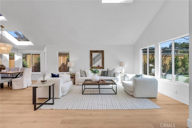 living area featuring a skylight, light wood finished floors, a wealth of natural light, and high vaulted ceiling