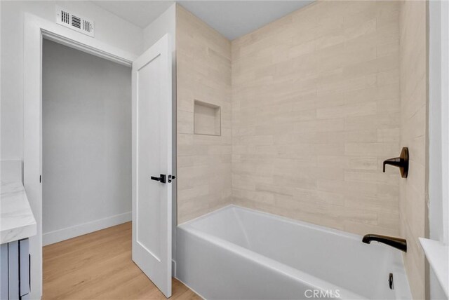 bathroom featuring wood finished floors, visible vents, vanity, baseboards, and bathtub / shower combination