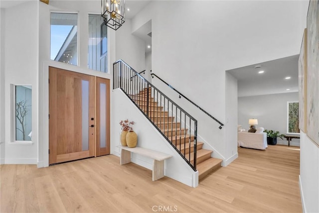 entrance foyer featuring a towering ceiling, an inviting chandelier, wood finished floors, and stairs