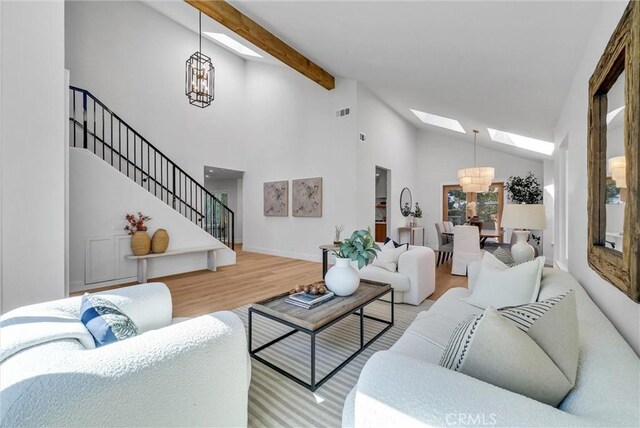 living room with stairway, beamed ceiling, a skylight, wood finished floors, and a notable chandelier