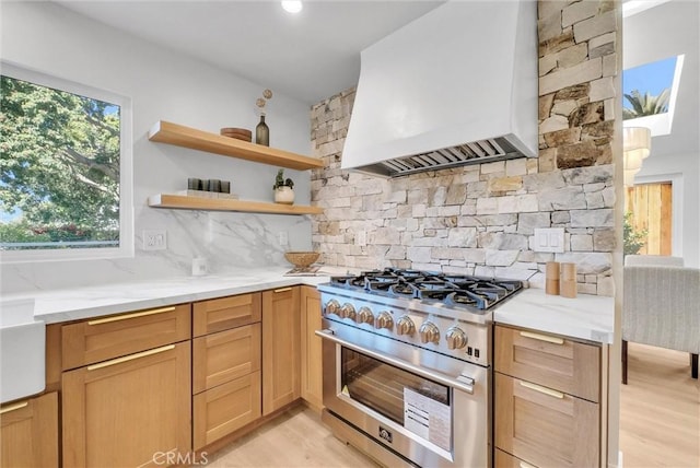 kitchen featuring light wood-style flooring, high end stove, decorative backsplash, light stone counters, and custom range hood