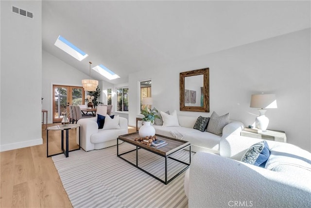 living area featuring visible vents, a skylight, baseboards, light wood-style flooring, and high vaulted ceiling