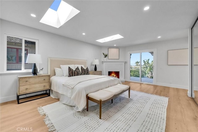 bedroom featuring a skylight, baseboards, light wood-type flooring, and access to exterior