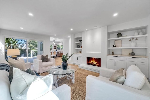 living room with built in features, light wood-style floors, a lit fireplace, and recessed lighting