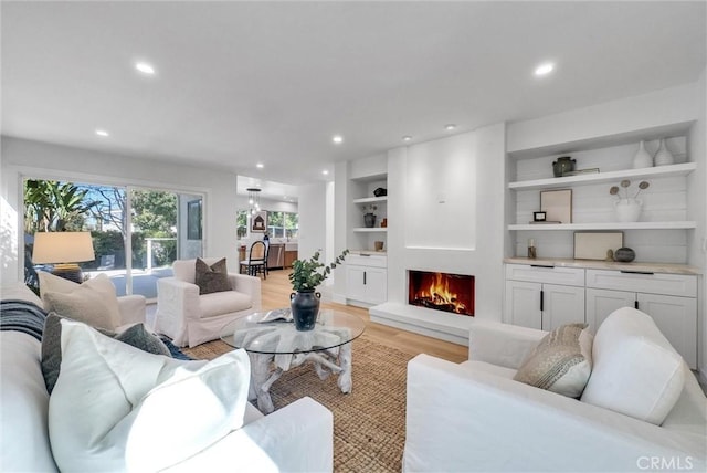 living room with recessed lighting, a warm lit fireplace, light wood-style flooring, and built in features