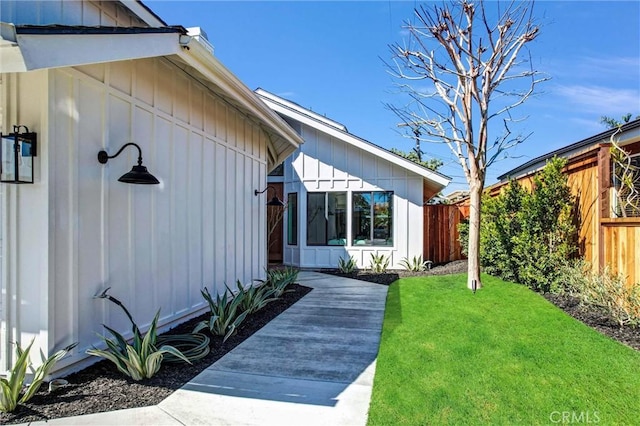 view of side of home featuring a lawn, board and batten siding, and fence