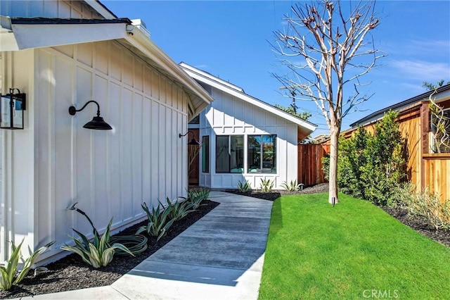 property entrance featuring board and batten siding, a lawn, and fence