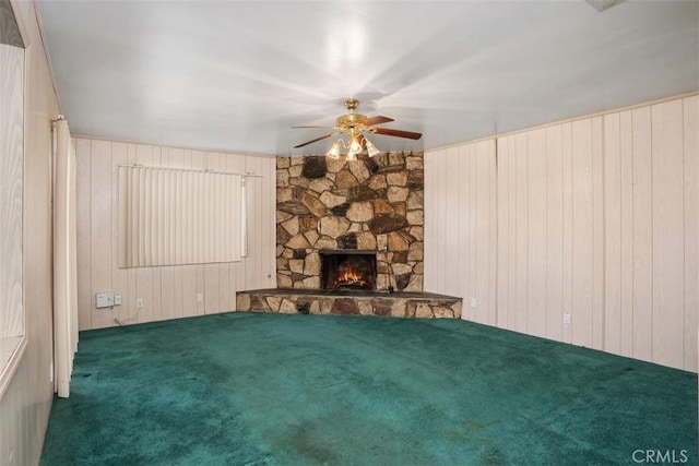 unfurnished living room with carpet, wooden walls, a ceiling fan, and a stone fireplace