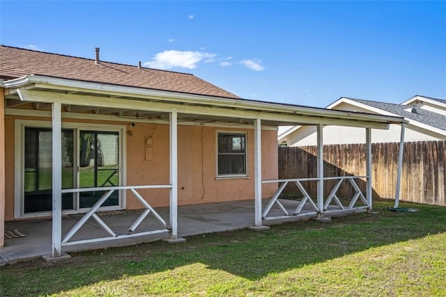 rear view of property with a yard, a shingled roof, fence, and stucco siding