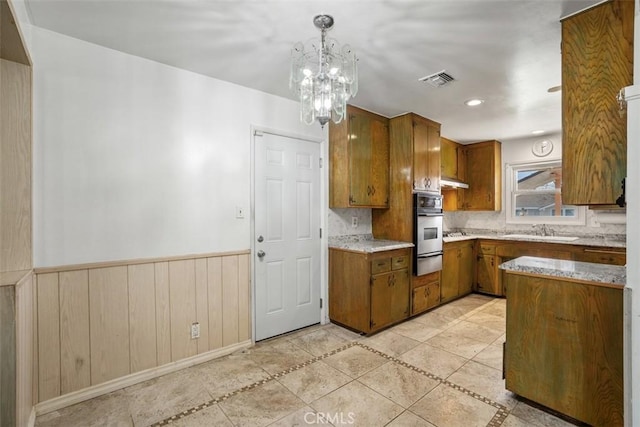 kitchen featuring a wainscoted wall, brown cabinets, a warming drawer, a sink, and oven