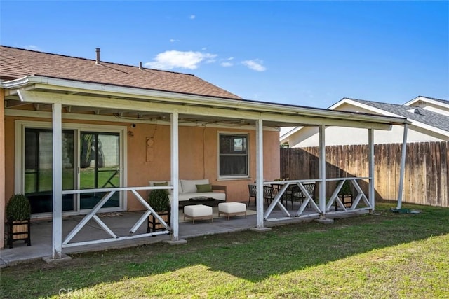 rear view of house featuring roof with shingles, fence, a lawn, and stucco siding