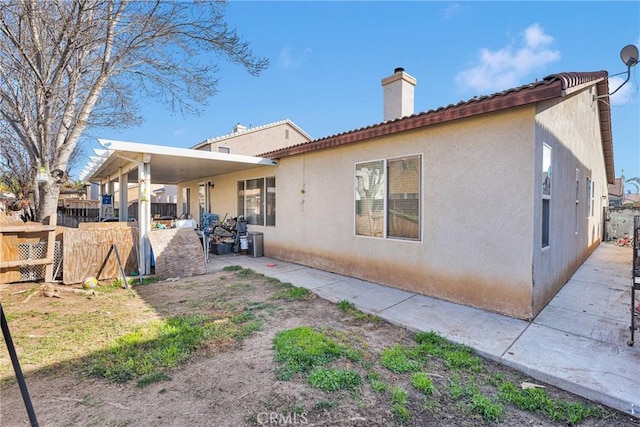 back of house with a patio area, a chimney, fence, and stucco siding