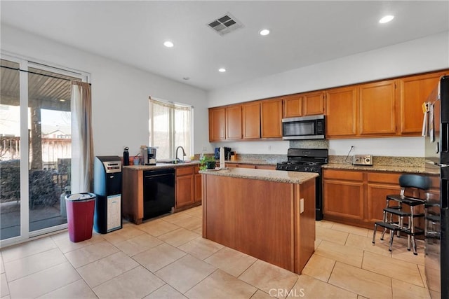 kitchen featuring light stone countertops, black appliances, a kitchen island, and visible vents