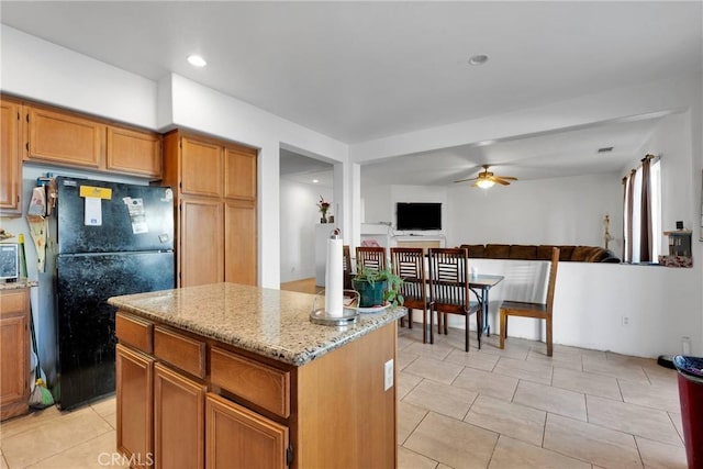 kitchen with ceiling fan, light stone countertops, open floor plan, freestanding refrigerator, and a center island