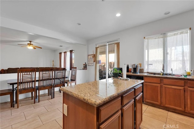 kitchen with light tile patterned floors, a sink, a kitchen island, light stone countertops, and brown cabinetry