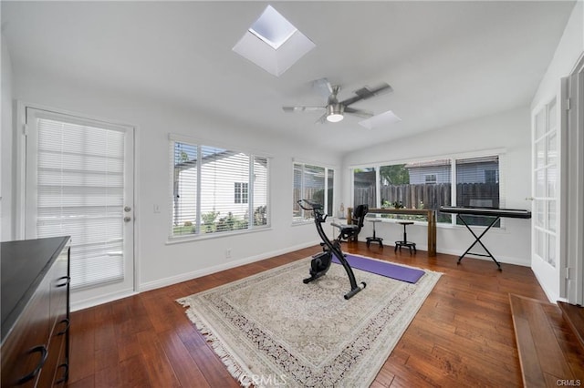 exercise area with dark wood-type flooring, vaulted ceiling with skylight, baseboards, and a ceiling fan