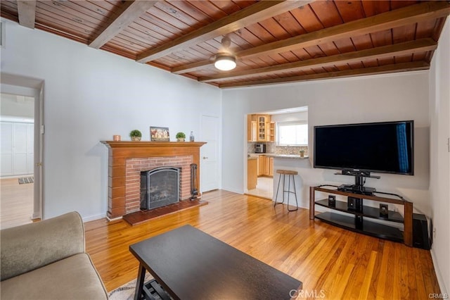 living area with wooden ceiling, baseboards, light wood-type flooring, a brick fireplace, and beam ceiling