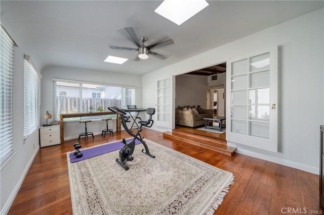 workout room with ceiling fan, hardwood / wood-style floors, a skylight, and baseboards