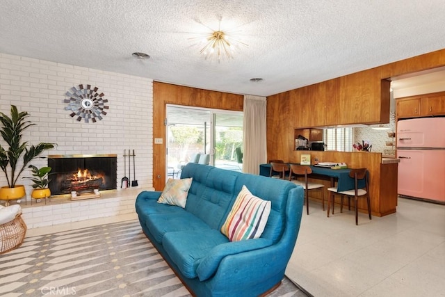 living area with a brick fireplace, a textured ceiling, and wood walls