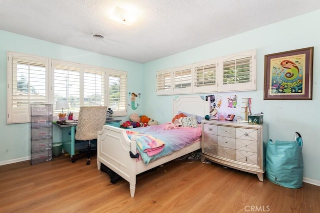 bedroom featuring light wood-style flooring, visible vents, baseboards, and a textured ceiling