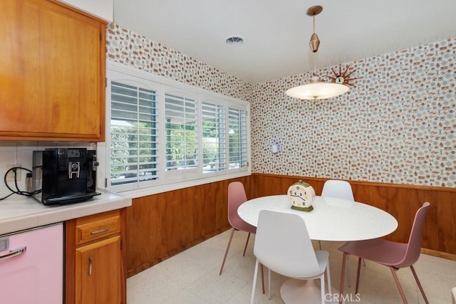 dining area featuring a wainscoted wall, light floors, visible vents, wood walls, and wallpapered walls