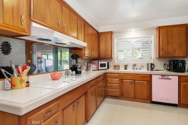 kitchen featuring brown cabinets, a sink, a peninsula, white appliances, and under cabinet range hood