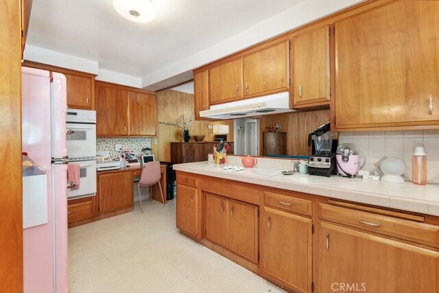 kitchen featuring light floors, brown cabinetry, backsplash, and white double oven