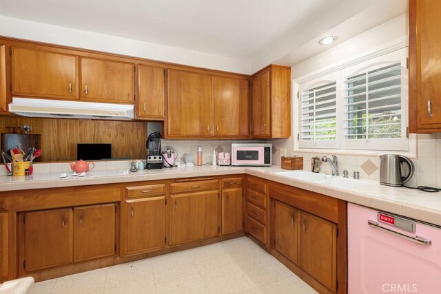 kitchen featuring decorative backsplash, white microwave, brown cabinetry, a sink, and under cabinet range hood