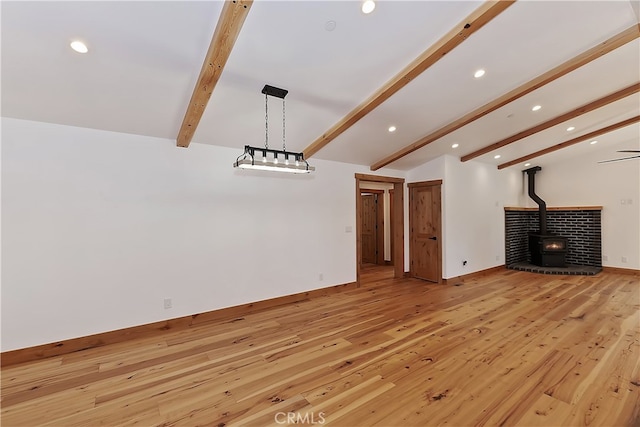 unfurnished living room with baseboards, lofted ceiling with beams, light wood-style flooring, a wood stove, and recessed lighting