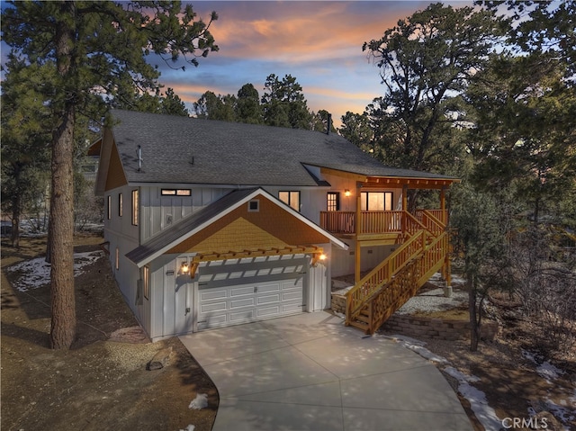 view of front of home featuring a shingled roof, board and batten siding, a garage, driveway, and stairs