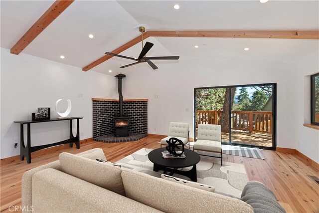 living area featuring beam ceiling, recessed lighting, a wood stove, wood finished floors, and baseboards