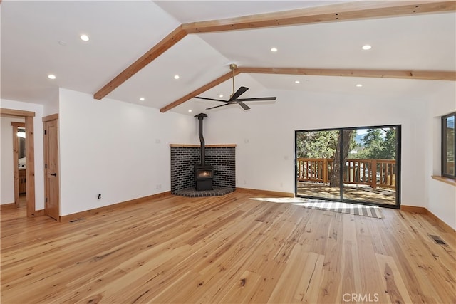 unfurnished living room featuring light wood finished floors, baseboards, visible vents, a wood stove, and beam ceiling