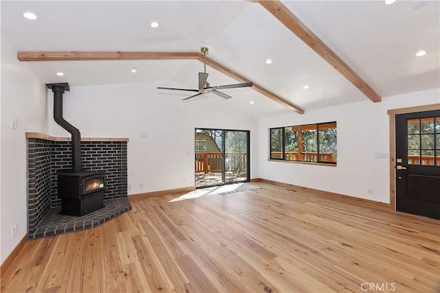 unfurnished living room with a wood stove, light wood-style floors, lofted ceiling with beams, and baseboards