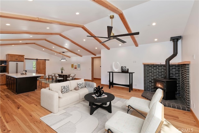 living room with light wood finished floors, lofted ceiling with beams, a barn door, a wood stove, and ceiling fan