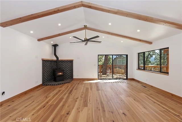 unfurnished living room featuring a wood stove, light wood-type flooring, baseboards, and beam ceiling