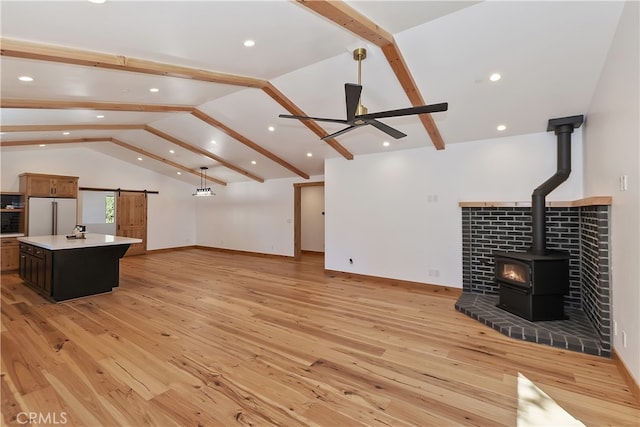 unfurnished living room with a barn door, a ceiling fan, a wood stove, light wood-type flooring, and beamed ceiling