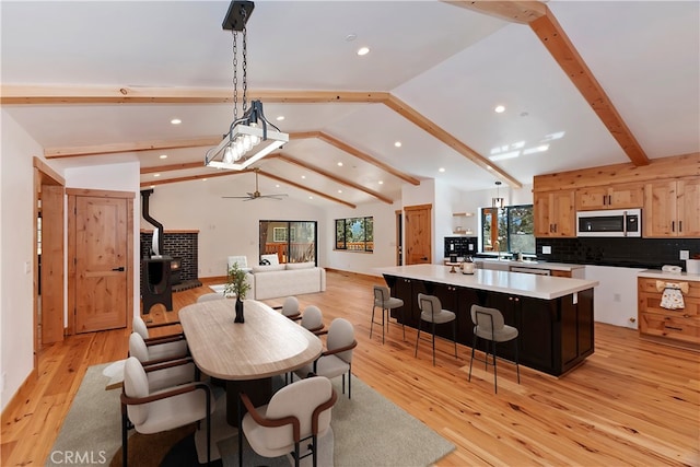 dining area featuring vaulted ceiling with beams, recessed lighting, light wood-style flooring, a ceiling fan, and a wood stove