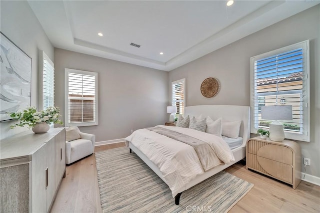 bedroom with light wood-type flooring, baseboards, a raised ceiling, and recessed lighting