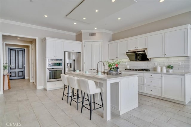 kitchen with visible vents, white cabinets, a kitchen breakfast bar, stainless steel appliances, and backsplash