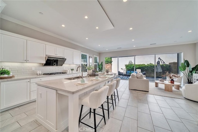 kitchen with crown molding, backsplash, open floor plan, white cabinets, and a sink