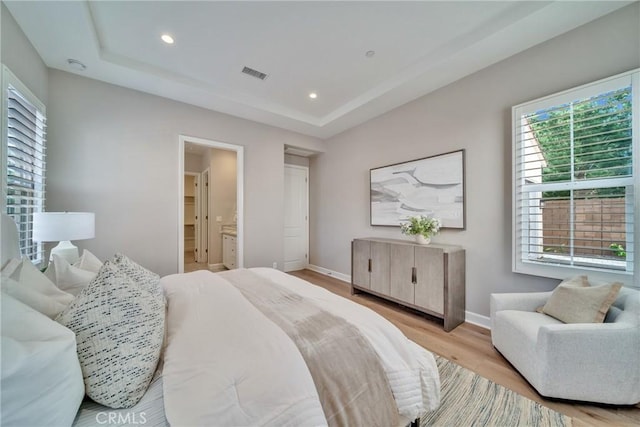 bedroom with light wood-type flooring, a tray ceiling, visible vents, and baseboards