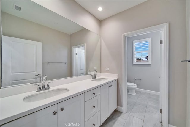 bathroom featuring toilet, double vanity, a sink, and visible vents