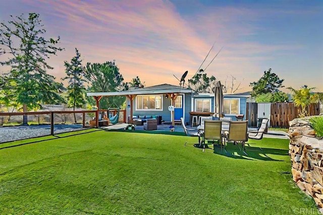 back of house at dusk featuring a patio area, a lawn, fence, and an outdoor living space