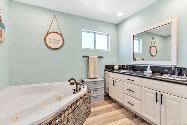 bathroom featuring double vanity, a jetted tub, wood finished floors, and a sink