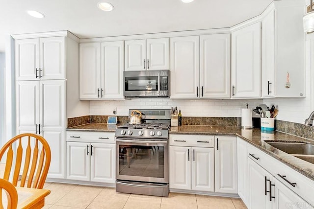 kitchen with a sink, white cabinetry, dark stone counters, appliances with stainless steel finishes, and decorative backsplash