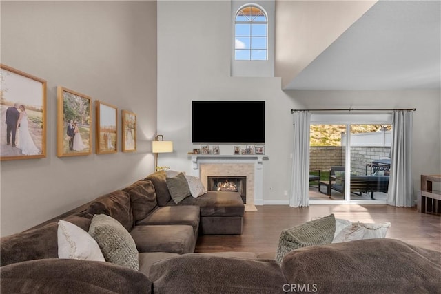 living room with a warm lit fireplace, a high ceiling, baseboards, and wood finished floors