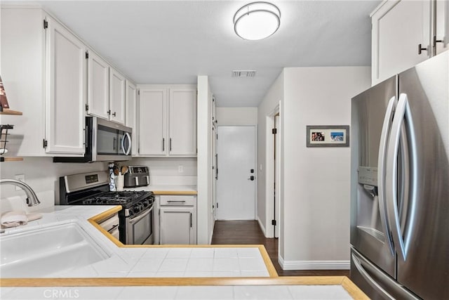 kitchen featuring visible vents, appliances with stainless steel finishes, white cabinets, a sink, and baseboards